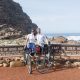 This photo shows two adventure cyclists, Emily Conrad-Pickles and James Davis as they stand next to the famous sign at the Cape of Good Hope.