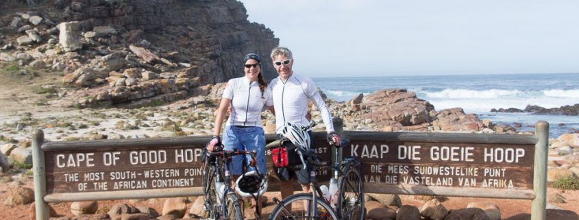 This photo shows two adventure cyclists, Emily Conrad-Pickles and James Davis as they stand next to the famous sign at the Cape of Good Hope.